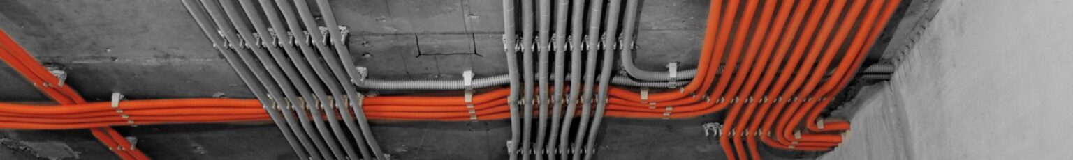 Кабельные трассы по потолку: оранжевые и серые линии в гофре, закреплённые с равным шагом